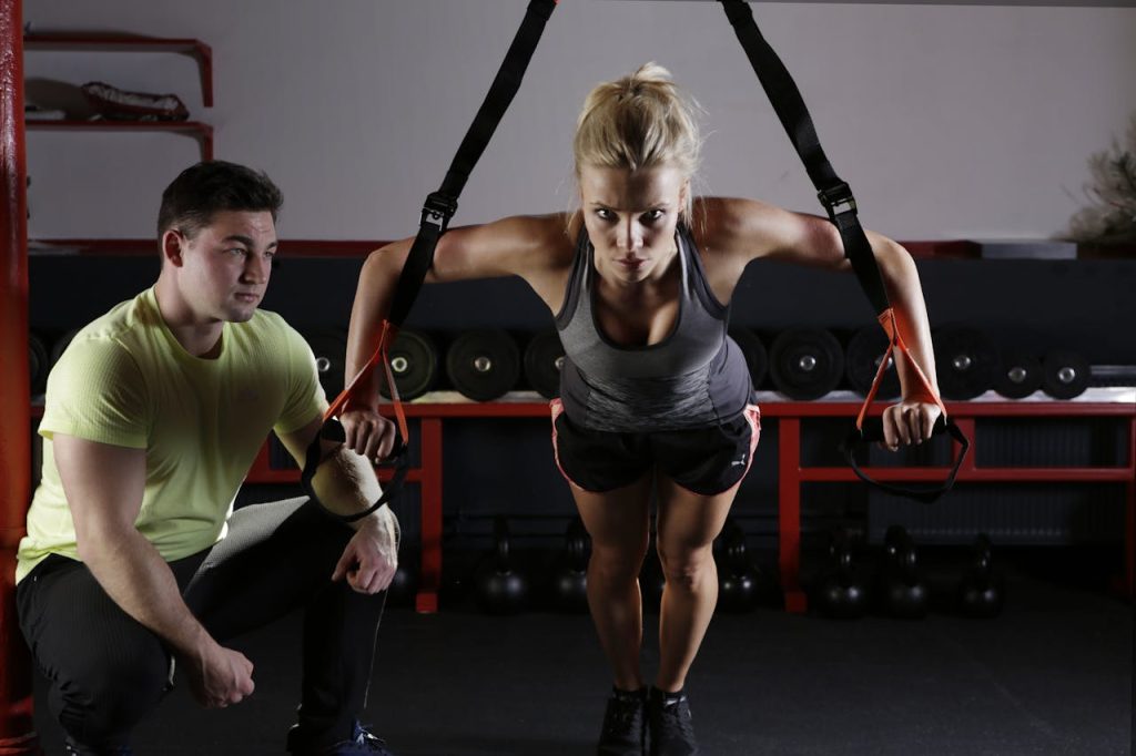 pexels-photo-414029 A woman performing strength training with a trainer in a gym setting, showcasing fitness and dedication.